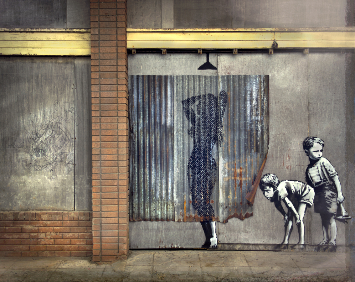The shower scene from Banksy's Dismaland where on a piece of street art two children are looking at a lady showering behind some corrugated iron